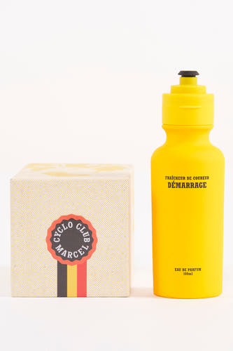 Gele parfum van Cyclo Club Marcel, in de vorm van een bidon met een zwarte dop, naast een doos.
