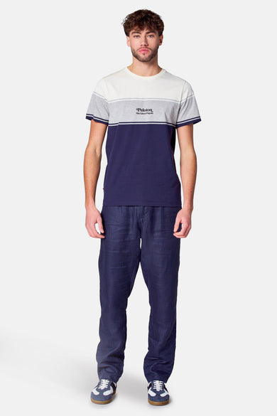 Multikleurig T-shirt met korte mouwen van Cyclo Club Marcel, met kleurblokken en donkerblauwe linnen broek en sneakers.
