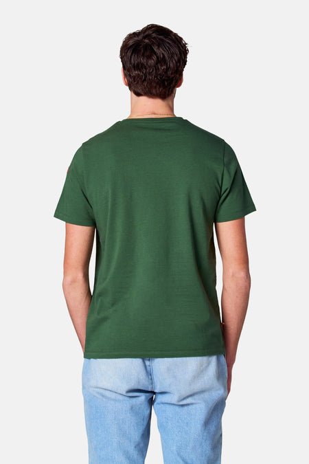 T-shirt vert avec manches courtes de Cyclo Club Marcel, vu de dos avec une chaîne d'or et un léger jean.