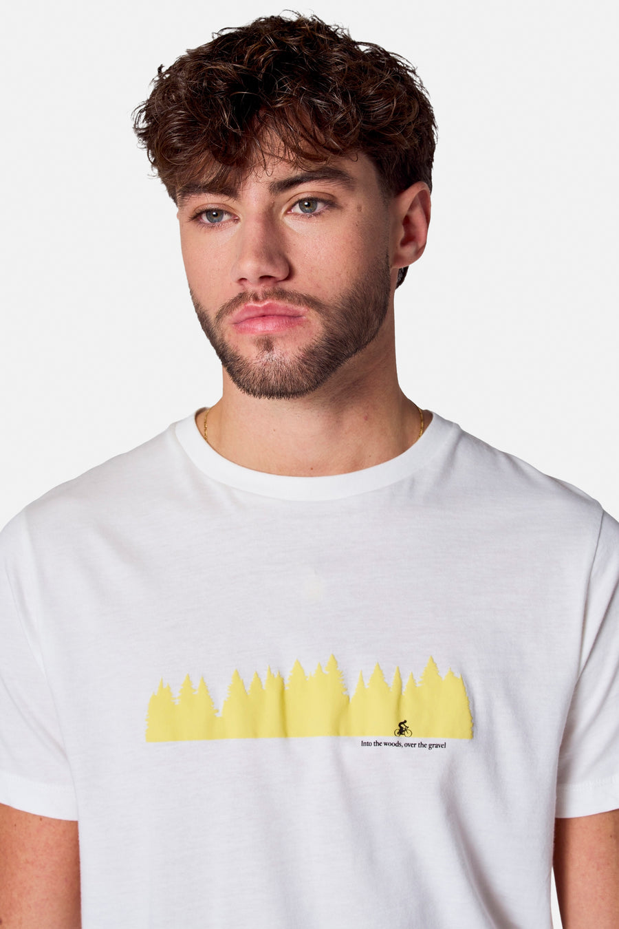 Wit T-shirt met korte mouwen van Cyclo Club Marcel, met een gele bosprint en de tekst "Into the woods, over the gravel".
