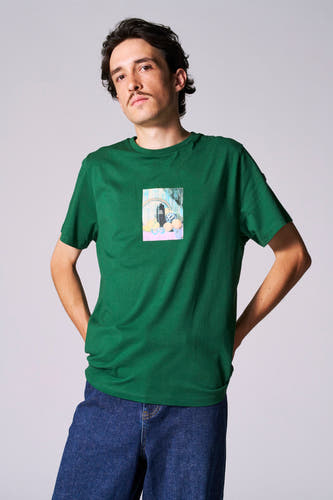 Groen T-shirt met korte mouwen van Cyclo Club Marcel, met een print op de borst, gedragen met een blauwe jeans.
