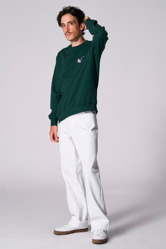 Sweater vert de Cyclo Club Marcel, porté avec un pantalon blanc et des baskets blanches à semelles brunes.