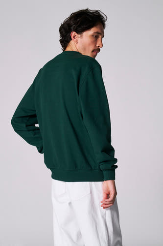 Pull-over vert avec col rond de Cyclo Club Marcel, porté avec un pantalon blanc.