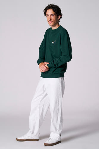 Pull-over vert de Cyclo Club Marcel, avec logo sur la poitrine, associé à un pantalon blanc et des baskets.