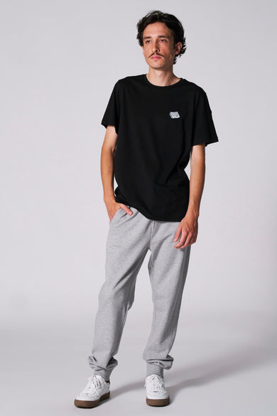 Zwart T-shirt met korte mouwen van Cyclo Club Marcel, met klein logo, gedragen met grijze joggingbroek en witte sneakers.

