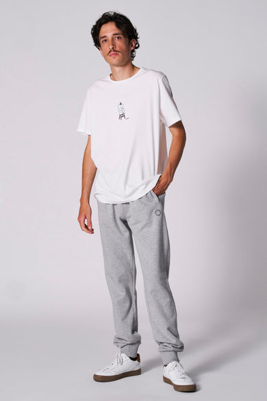 Man met wit T-shirt en grijze joggingbroek, staand.
