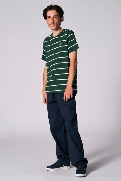 Groen gestreept T-shirt met korte mouwen van Cyclo Club Marcel, gedragen met donkerblauwe broek en sneakers.
