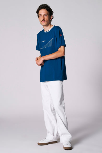 Blauw T-shirt met korte mouwen van Cyclo Club Marcel, met witte grafische print en witte broek en schoenen.
