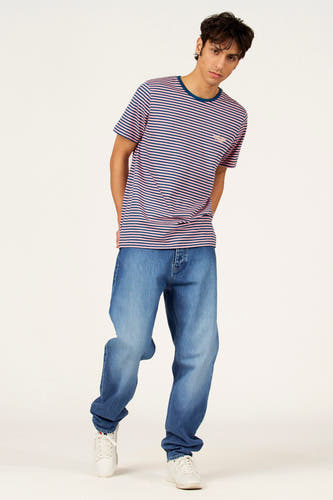 Multikleurig T-shirt met korte mouwen van Cyclo Club Marcel, met blauw-roze strepen, losse jeans en witte sneakers.
