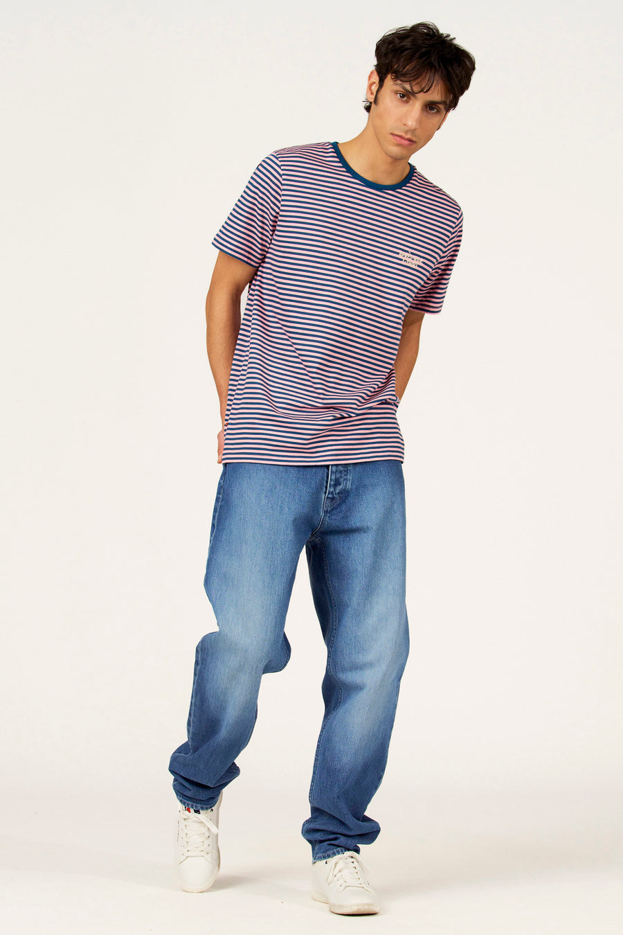 Multikleurig T-shirt met korte mouwen van Cyclo Club Marcel, met blauw-roze strepen, losse jeans en witte sneakers.
