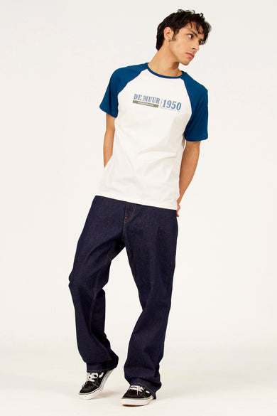Wit T-shirt met korte mouwen van Cyclo Club Marcel, met blauwe raglanmouwen, gedragen met donkerblauwe jeans en zwarte sneakers.
