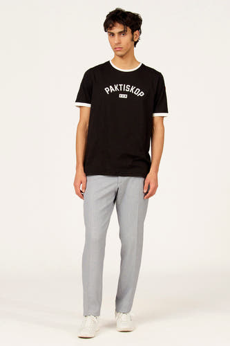 T-shirt à manches courtes noir de Cyclo Club Marcel, avec col et poignets blancs, porté avec un pantalon gris et des baskets blanches.