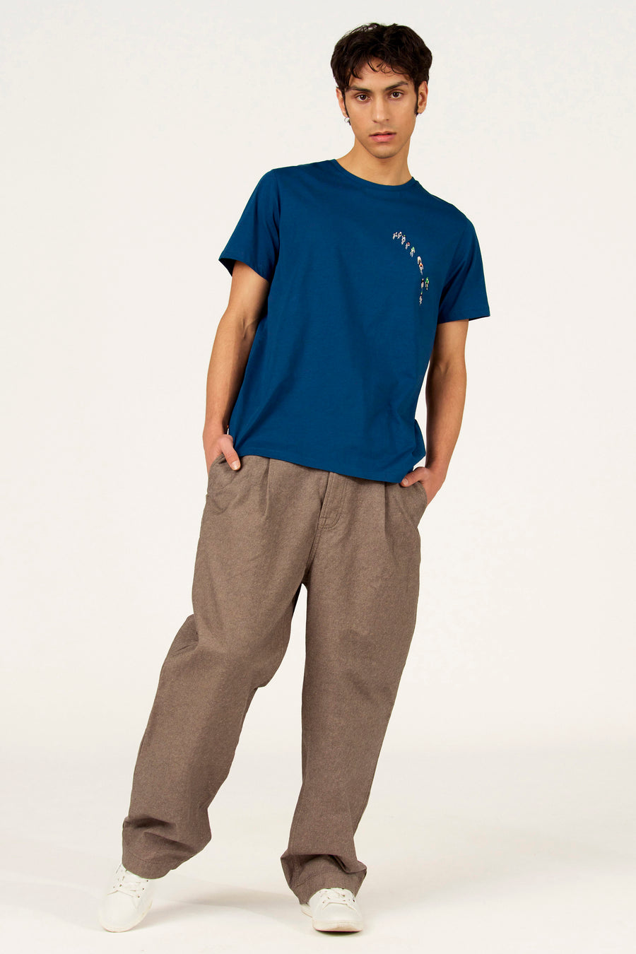 T-shirt bleu à manches courtes de Cyclo Club Marcel, avec imprimé de cyclistes, combiné avec un pantalon marron et des chaussures blanches.