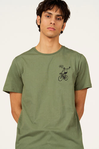 T-shirt vert à manches courtes de Cyclo Club Marcel, avec un écusson logo sur la manche, porté avec un pantalon rayé.