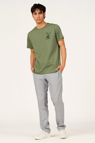T-shirt vert à manches courtes de Cyclo Club Marcel, avec un petit imprimé d'un cycliste et porté avec un pantalon gris et des chaussures blanches.