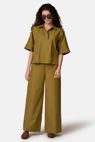 Groene broek van COPINES D'ANVERS met wijde pijpen, gecombineerd met een bijpassend shirt, zonnebril en loafers met slangenprint.