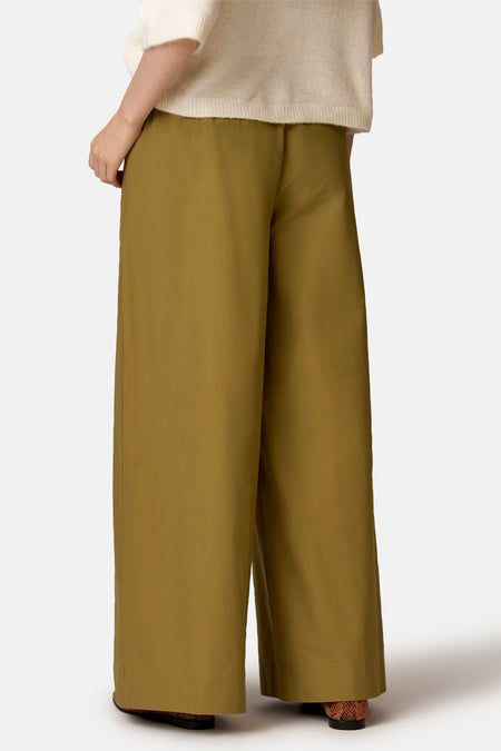 Groene broek van COPINES D'ANVERS met wijde pijpen, vanuit de achterkant gezien, gedragen met een beige trui en bruine slangenleren schoenen.