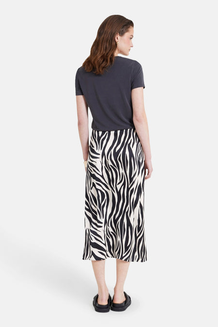 Lange, veelkleurige rok van NAF NAF met een zebraprint, gecombineerd met een grijs T-shirt en zwarte sandalen.
