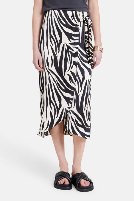 Lange, meerkleurige rok van NAF NAF, met een opvallend zebraprint en gekruiste, zwarte sandalen.
