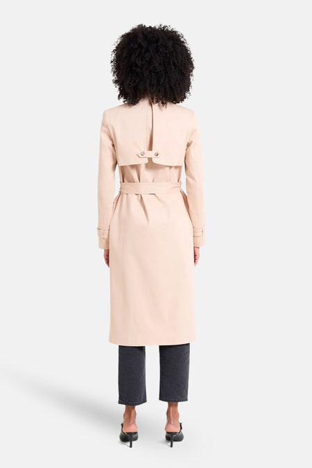 Beige lange jas van NAF NAF, gezien van achteren, gecombineerd met donkere jeans en zwarte hakken.
