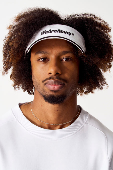 Chapeau blanc de Coely avec le texte "WeAreMany" et un bord noir, porté avec un t-shirt blanc et une chaîne d'argent.