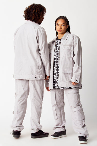 Grijze korte jas van COELY, met opgestikte zakken en gedragen met een broek met cargozakken.
