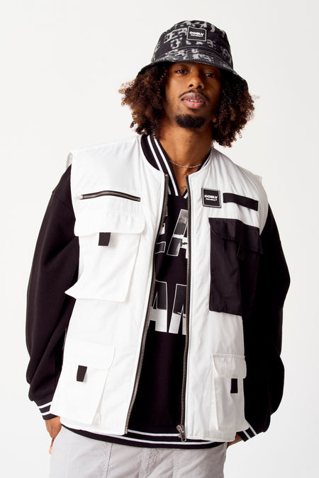 Veste blanche de COELY, avec des poches et des accents noirs, portée sur un pull noir et une chemise imprimée.