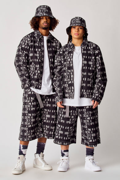 Zwarte korte jas van COELY, met een opvallend wit patroon, gecombineerd met bijpassende shorts en bucket hat.
