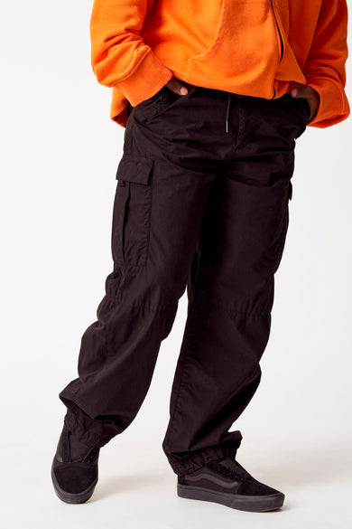 Zwarte cargobroek van COELY, met cargozakken en trekkoord, gecombineerd met een oranje hoodie en zwarte sneakers.

