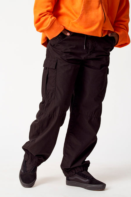 Zwarte cargobroek van COELY, met cargozakken en trekkoord, gecombineerd met een oranje hoodie en zwarte sneakers.
