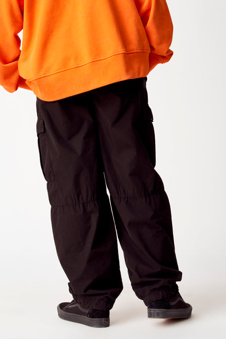 Zwarte cargobroek van COELY, met losse pasvorm en zakken op de benen, gecombineerd met een oranje hoodie en zwarte sneakers.
