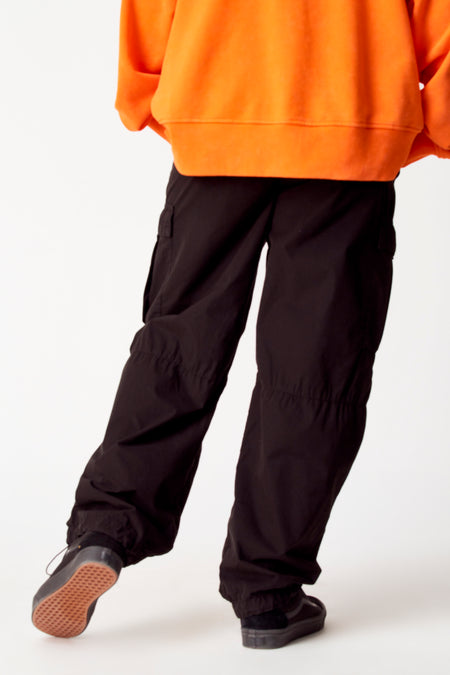 Zwarte cargobroek van COELY, gedragen met een oranje trui en zwarte sneakers met bruine zolen.
