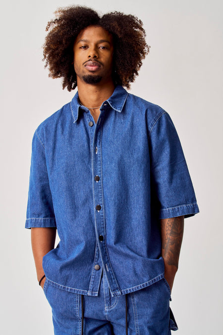 Blauw jeanshemd van COELY, met korte mouwen en zwarte knopen.