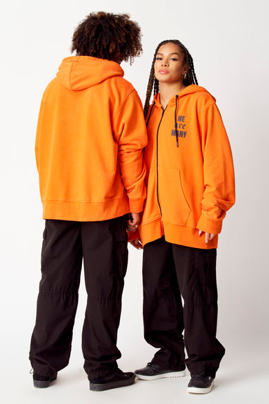 Oranje sweater met kap van COELY, gedragen met zwarte broek en sneakers.