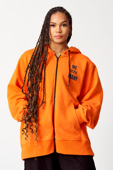 Oranje sweater met kap van COELY, met zwarte rits en tekstprint "WE are MANY" op de borst.