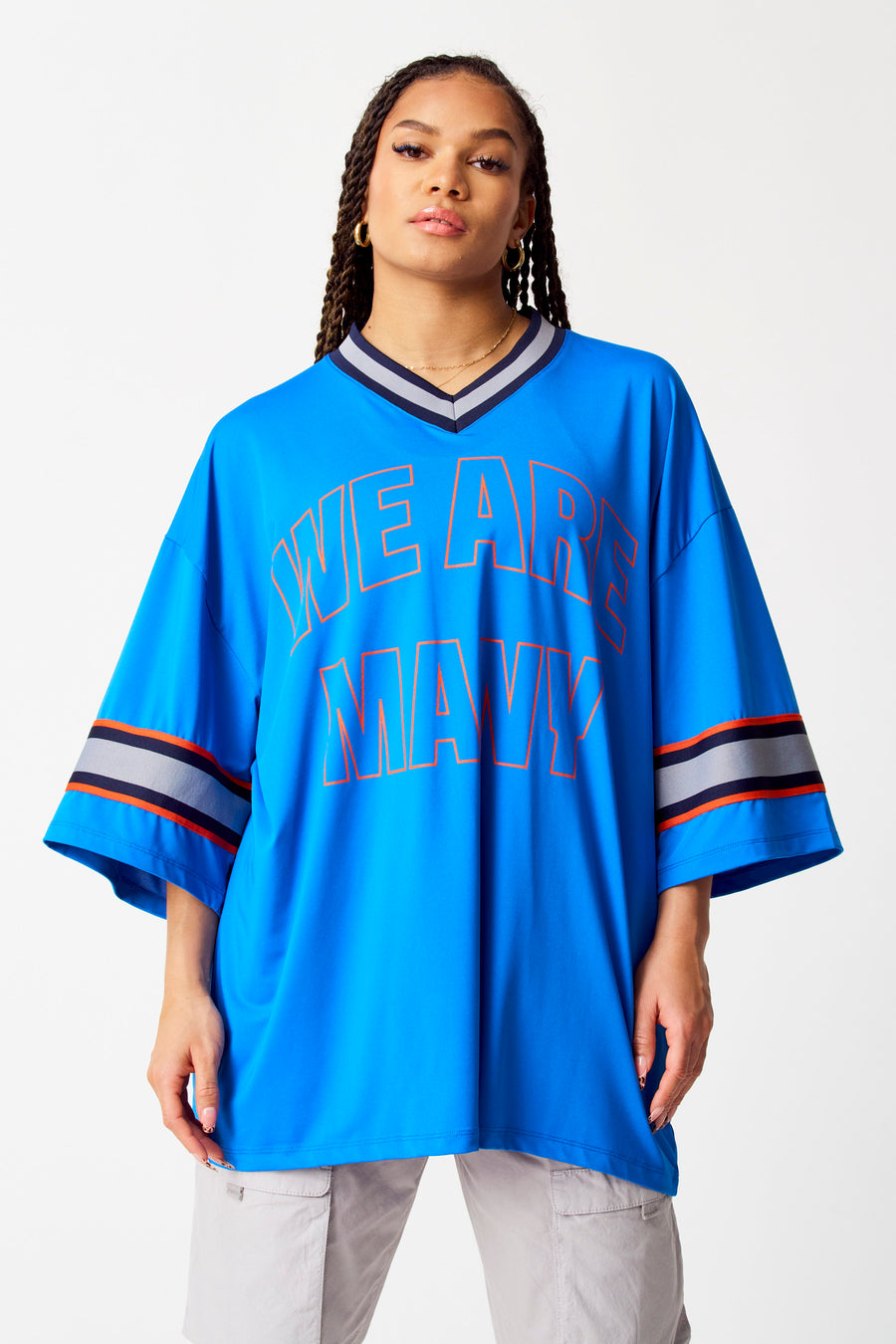 Blauwe top van COELY, met oranje opdruk en gestreepte details bij de mouwen, gedragen met een grijze broek.

