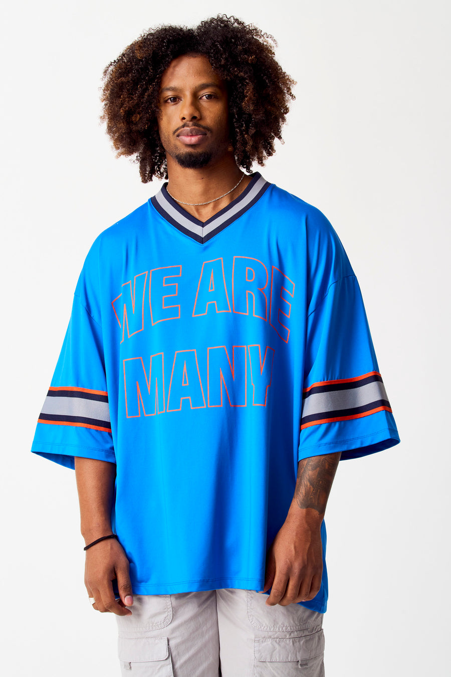 Blauwe top van COELY met korte mouwen en de tekst "WE ARE MANY" erop, gedragen met een ketting en cargobroek.
