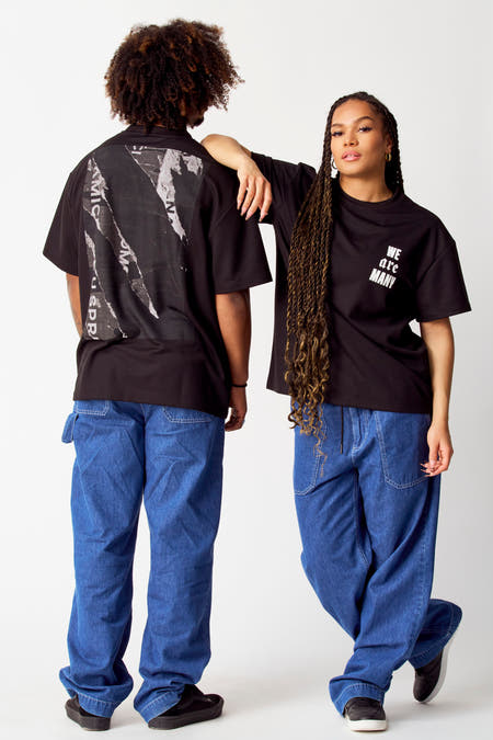 Zwart T-shirt van COELY, met print op de achterkant en opschrift 'We are Many' op de voorkant, gedragen met jeans.
