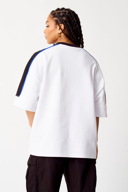 Sweater blanc de COELY, avec des rayures noires et bleues sur les manches, porté avec un pantalon noir, vue arrière.