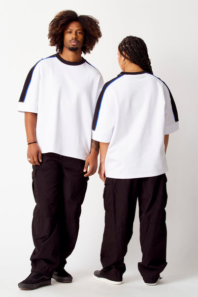 Pullis blanc avec col rond de COELY, avec des rayures noires et bleues sur les manches, porté avec un pantalon cargo noir.