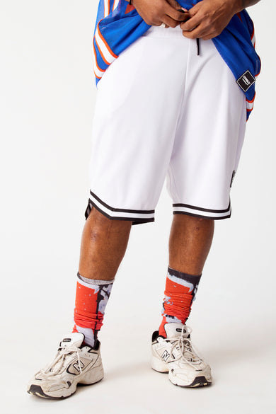 Short blanc de COELY, avec une bande noire en bas, porté avec des chaussettes rouges et des baskets blanches.