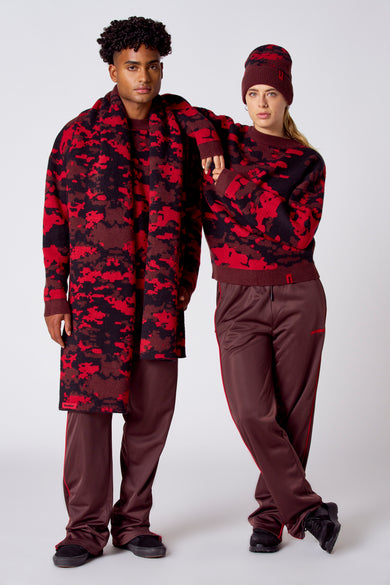 Multicolor muts van COELY, met een rood en zwart camouflagepatroon, gedragen met een bijpassende trui en broek.
