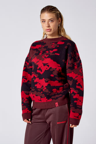Rode trui met ronde hals van COELY, met een rood en zwart camouflagepatroon, gecombineerd met bruine joggingbroek.
