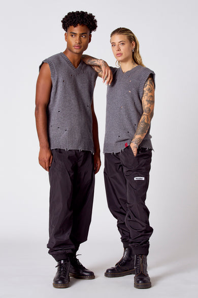 Veste grise de COELY, avec des trous, portée avec un pantalon noir et des bottes noires.