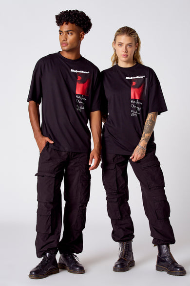 T-shirt noir à manches courtes de COELY, avec une impression rouge et un texte à porter, associé à des pantalons cargo noirs et des bottes militaires.