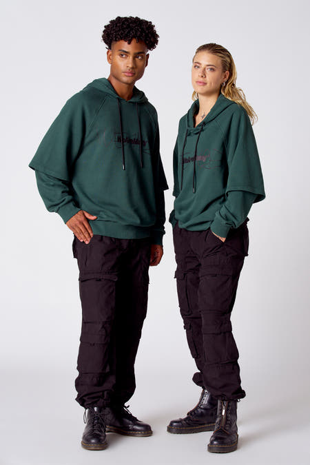 Groene sweatshirt met kap van COELY, met zwarte trekkoorden, gecombineerd met zwarte cargo broek en zwarte laarzen.