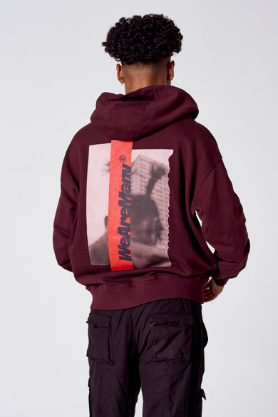 Bordeauxkleurige sweater met kap van COELY, met een grafische print op de rug en gedragen met donkere cargobroeken.