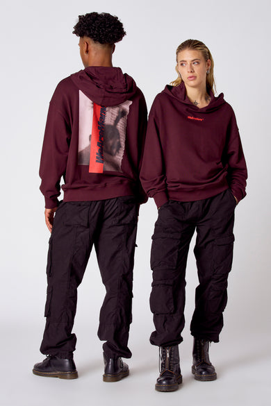 Bordeauxkleurige sweater met kap van COELY, met print op de rug en gecombineerd met zwarte cargo broek en zwarte boots.
