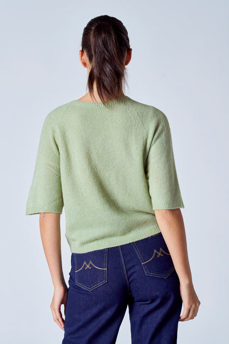 Groene trui met ronde hals van Clouds of Fashion, rugzijde getoond, gecombineerd met donkere jeans met decoratieve zakken.
