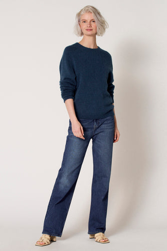 Blauwe trui met ronde hals van Clouds of Fashion, gecombineerd met donkerblauwe jeans en beige sandalen.
